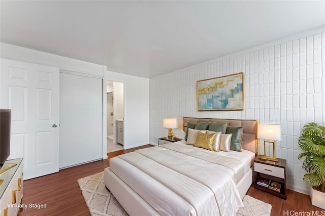 bedroom with dark wood-type flooring, tile walls, and ensuite bath