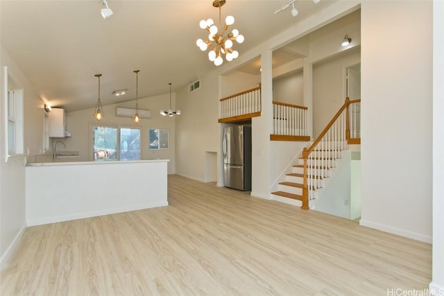 kitchen with sink, kitchen peninsula, stainless steel fridge, white cabinets, and light wood-type flooring