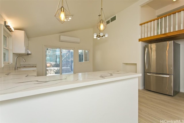 kitchen featuring stainless steel fridge, light stone counters, sink, pendant lighting, and white cabinetry