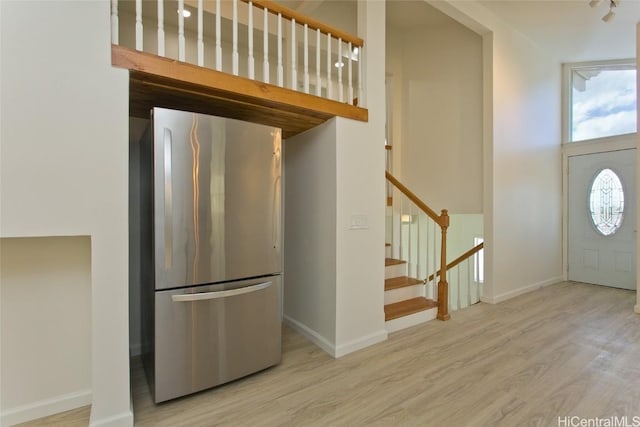 kitchen featuring light hardwood / wood-style floors, a towering ceiling, and stainless steel refrigerator