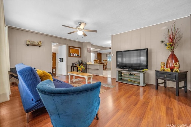 living room featuring ceiling fan, hardwood / wood-style floors, and wood walls