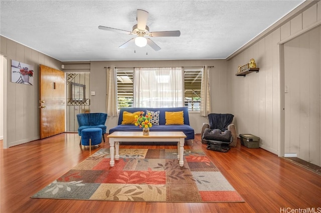 living room with wood-type flooring, a textured ceiling, ceiling fan, and wooden walls