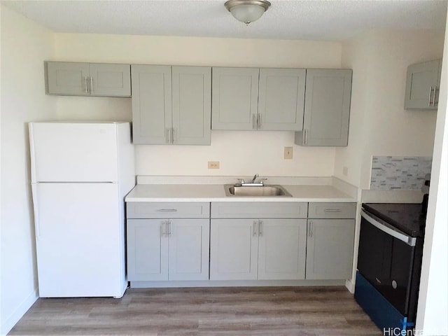 kitchen with gray cabinetry, electric range, sink, white fridge, and light wood-type flooring