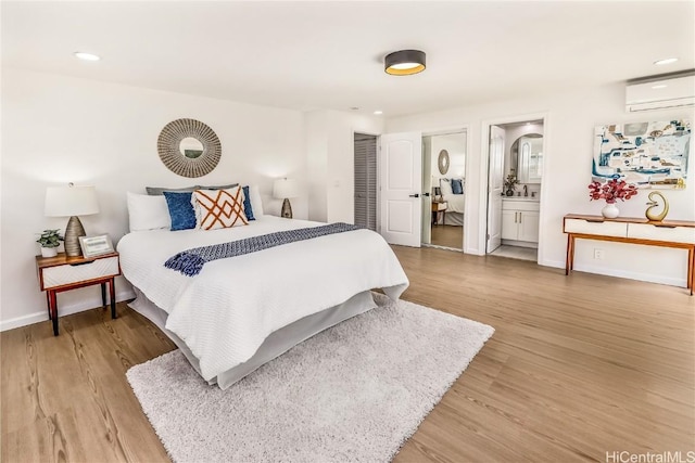 bedroom with a wall mounted air conditioner, light hardwood / wood-style floors, and ensuite bath