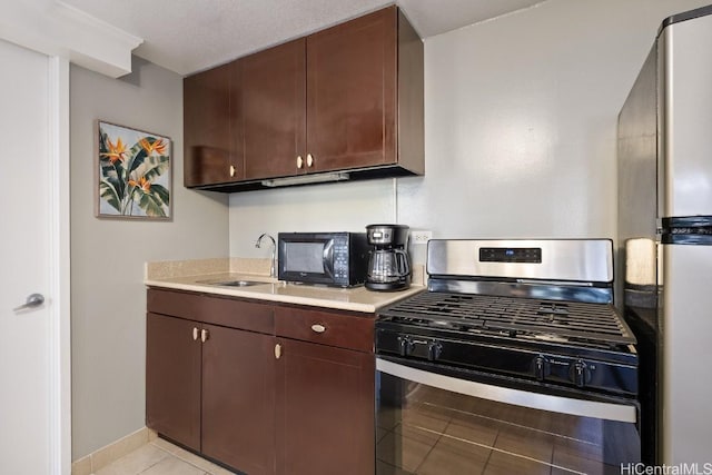 kitchen featuring sink, gas range oven, light tile patterned floors, stainless steel refrigerator, and dark brown cabinets