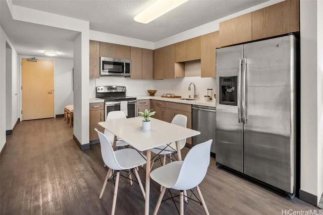 kitchen with light countertops, stainless steel appliances, wood finished floors, a textured ceiling, and a sink