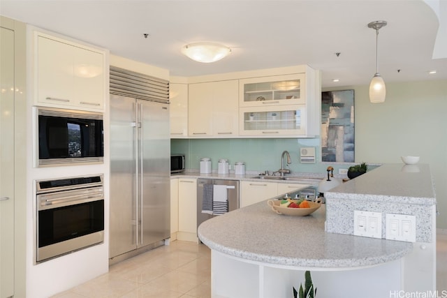 kitchen with decorative light fixtures, a peninsula, built in appliances, a sink, and light tile patterned flooring