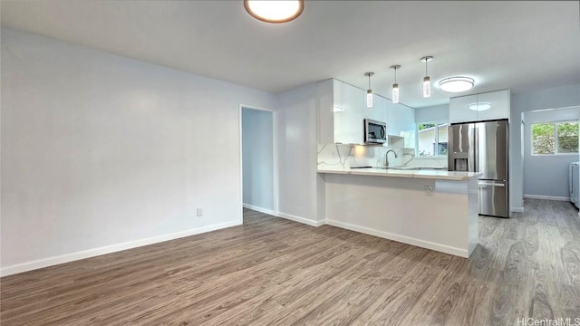 kitchen with kitchen peninsula, light wood-type flooring, stainless steel appliances, decorative light fixtures, and white cabinetry