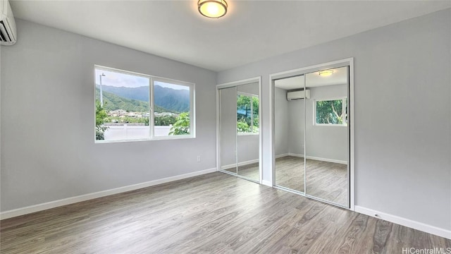 unfurnished bedroom featuring a mountain view, a wall mounted air conditioner, hardwood / wood-style flooring, and multiple closets