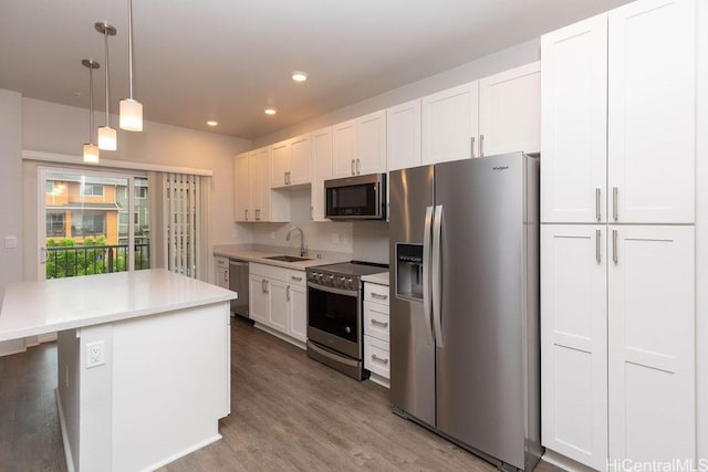 kitchen with white cabinetry, sink, hanging light fixtures, appliances with stainless steel finishes, and hardwood / wood-style flooring