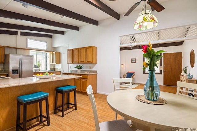 kitchen with a towering ceiling, a breakfast bar, beamed ceiling, light hardwood / wood-style floors, and stainless steel fridge with ice dispenser