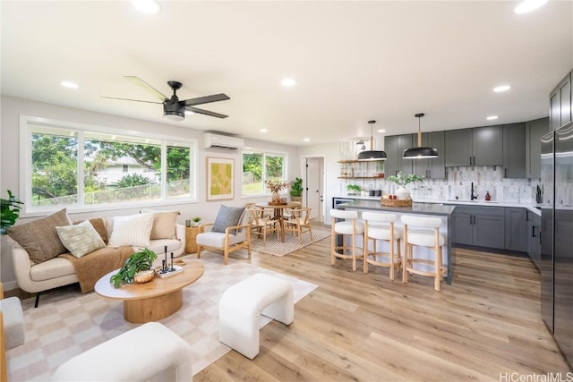 living room featuring ceiling fan, sink, a wall mounted air conditioner, and light wood-type flooring