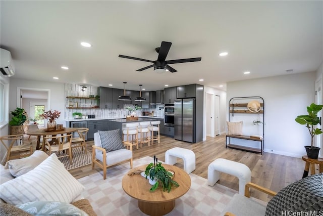 living room with a wall mounted air conditioner, ceiling fan, and light hardwood / wood-style floors