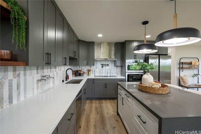 kitchen with wall chimney range hood, sink, light wood-type flooring, appliances with stainless steel finishes, and tasteful backsplash