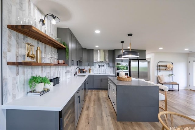 kitchen with gray cabinetry, hanging light fixtures, wall chimney range hood, light hardwood / wood-style flooring, and appliances with stainless steel finishes