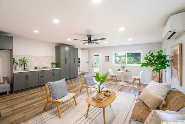 living room featuring ceiling fan, sink, a wall mounted air conditioner, and light wood-type flooring