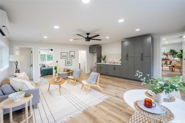 living room with ceiling fan, a wall unit AC, and light hardwood / wood-style flooring