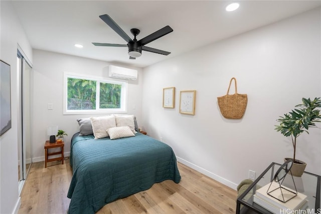 bedroom with a wall mounted air conditioner, ceiling fan, and light hardwood / wood-style floors