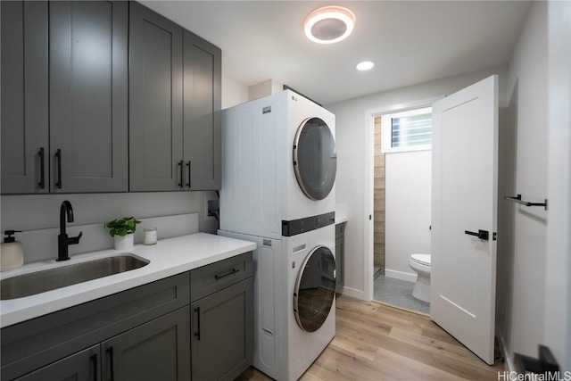 laundry area featuring sink, stacked washing maching and dryer, and light hardwood / wood-style flooring