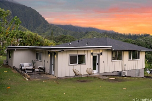 back house at dusk with a lawn, a mountain view, and a patio