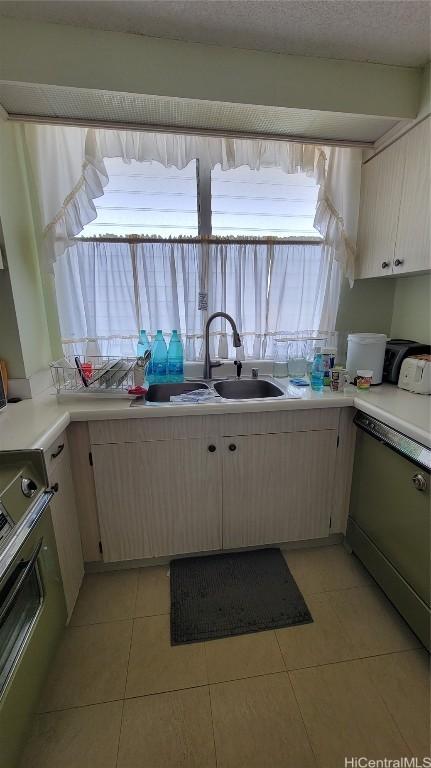 kitchen with stainless steel dishwasher, a wealth of natural light, sink, range, and light tile patterned flooring