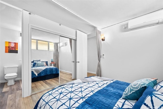 bedroom with ensuite bathroom, wood-type flooring, a wall mounted AC, and a closet