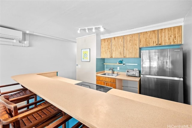 kitchen featuring track lighting, a kitchen breakfast bar, sink, stainless steel refrigerator, and a wall unit AC