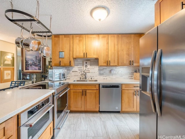 kitchen with appliances with stainless steel finishes, a textured ceiling, tasteful backsplash, and sink