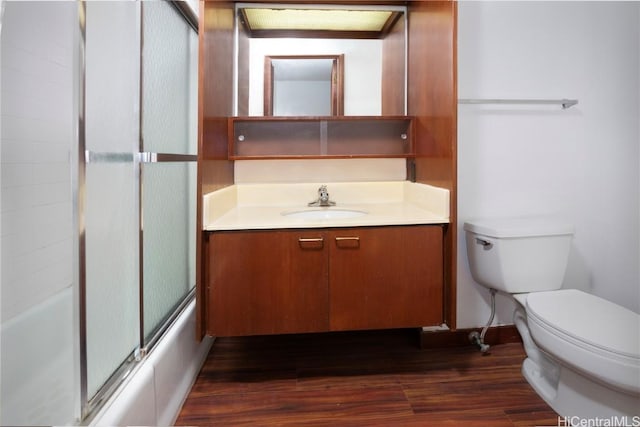 bathroom with vanity, toilet, wood finished floors, and bath / shower combo with glass door