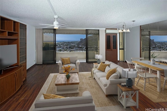 living room with dark wood-type flooring, a wall unit AC, ceiling fan with notable chandelier, and a textured ceiling