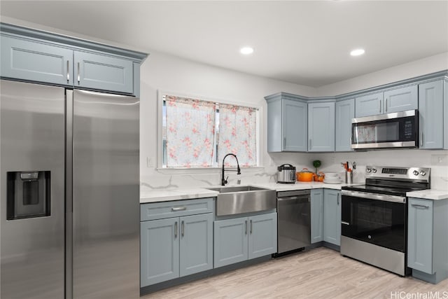 kitchen featuring light stone countertops, stainless steel appliances, light hardwood / wood-style flooring, and sink