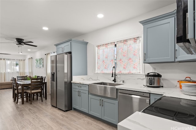 kitchen with sink, ceiling fan, light wood-type flooring, light stone counters, and stainless steel appliances