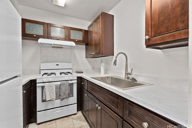 kitchen featuring dark brown cabinetry, sink, light tile patterned floors, and white appliances