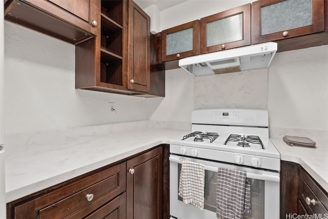 kitchen featuring dark brown cabinetry, light stone counters, and white gas stove