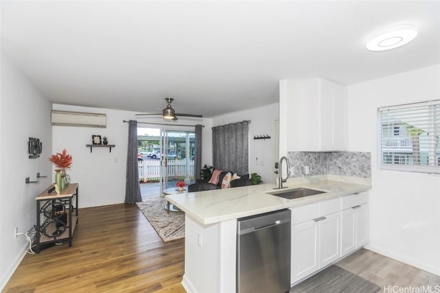 kitchen featuring a wall mounted air conditioner, kitchen peninsula, sink, stainless steel dishwasher, and white cabinetry