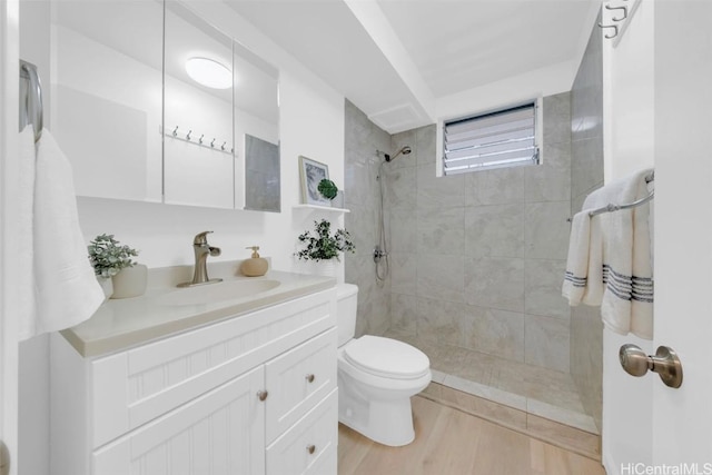 bathroom with hardwood / wood-style floors, vanity, a tile shower, and toilet