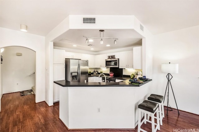 kitchen with dark wood-type flooring, white cabinets, appliances with stainless steel finishes, a kitchen bar, and kitchen peninsula