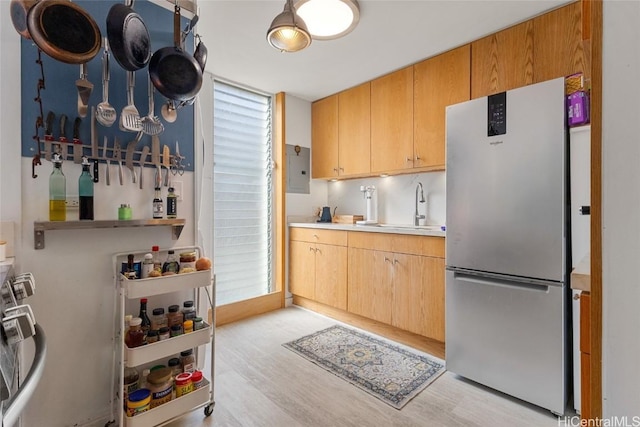 kitchen with electric panel, stainless steel fridge, sink, and light wood-type flooring