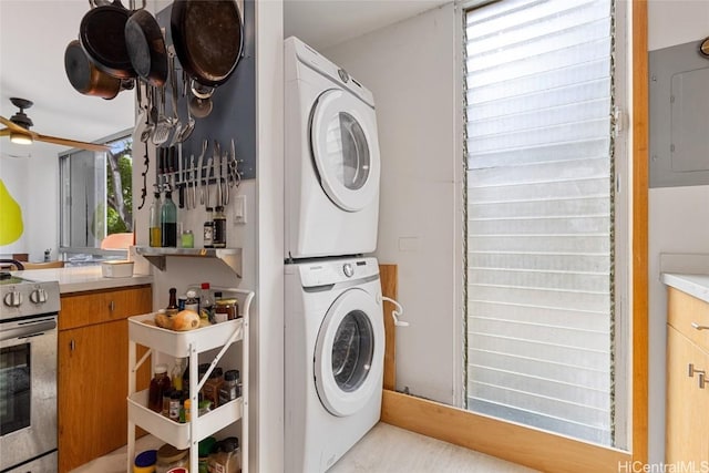 washroom with electric panel, a wealth of natural light, and stacked washing maching and dryer