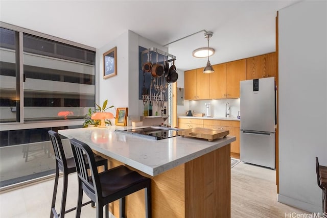 kitchen with a kitchen bar, stainless steel refrigerator, stovetop, and hanging light fixtures