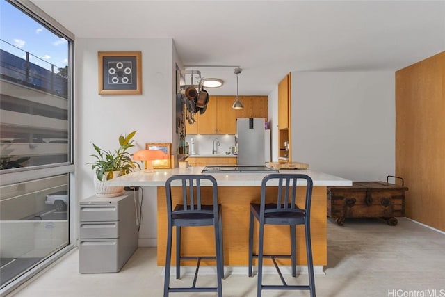 kitchen featuring pendant lighting, a kitchen breakfast bar, sink, kitchen peninsula, and stainless steel refrigerator