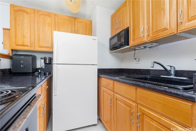 kitchen featuring white refrigerator, dark stone countertops, and sink