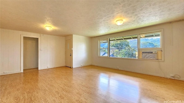 spare room featuring wood walls, cooling unit, a textured ceiling, and light wood-type flooring