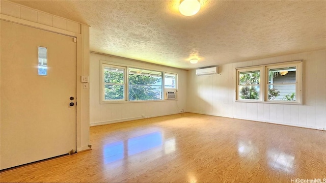 unfurnished room featuring a wall unit AC, light hardwood / wood-style flooring, and a textured ceiling