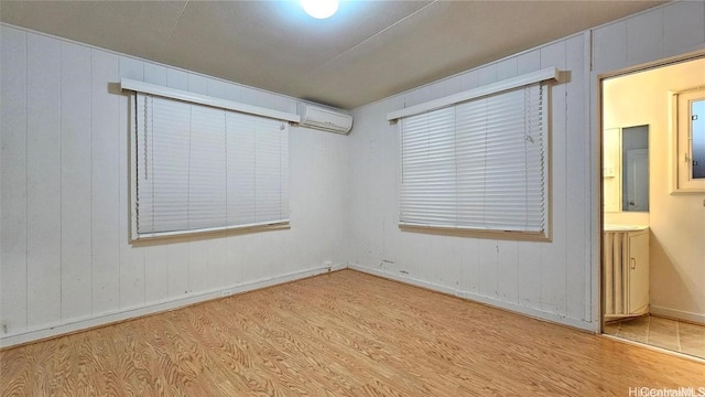 empty room featuring light hardwood / wood-style flooring, a wall unit AC, and wooden walls