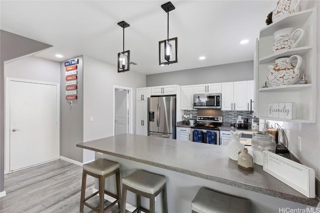 kitchen with white cabinetry, stainless steel appliances, light hardwood / wood-style flooring, kitchen peninsula, and a breakfast bar area