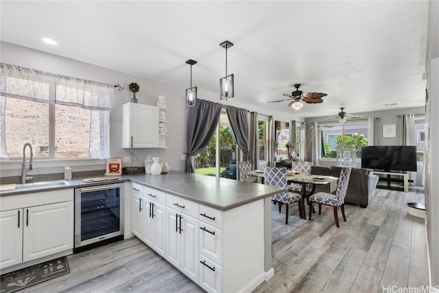 kitchen featuring white cabinetry, sink, beverage cooler, kitchen peninsula, and light hardwood / wood-style floors