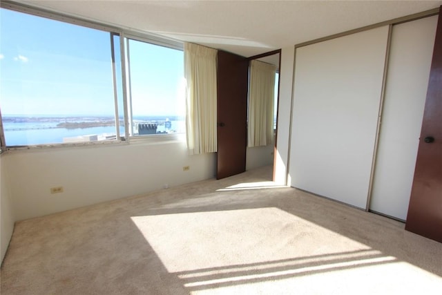 unfurnished bedroom featuring a water view and light colored carpet