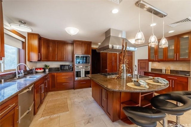 kitchen featuring appliances with stainless steel finishes, island range hood, a kitchen island with sink, sink, and dark stone countertops