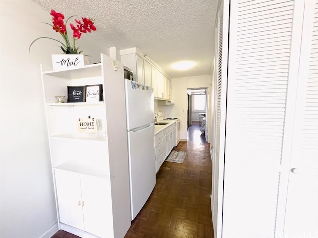 kitchen featuring freestanding refrigerator, white cabinetry, and a textured ceiling